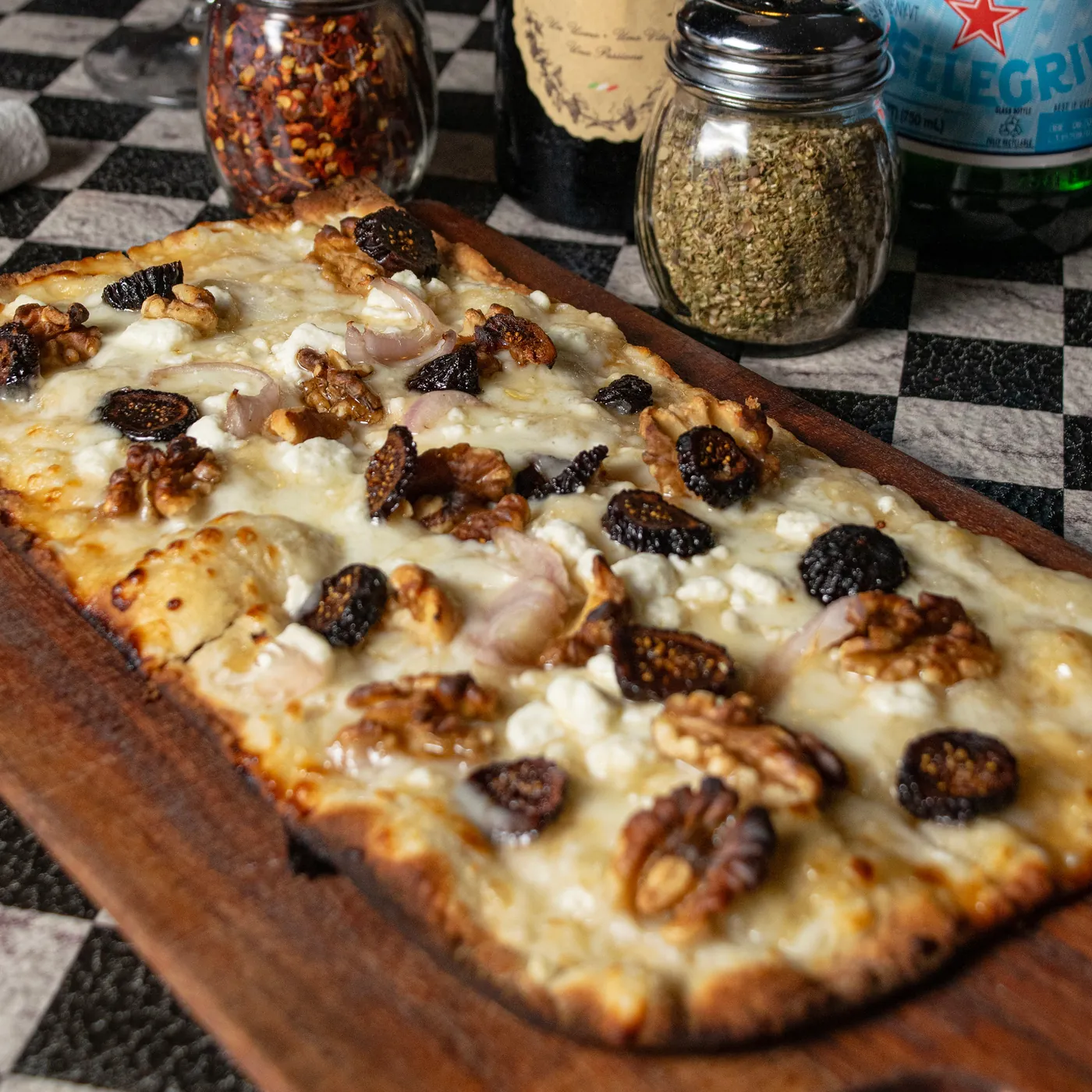 Fig and goat cheese flat bread with candied walnuts on a dark board