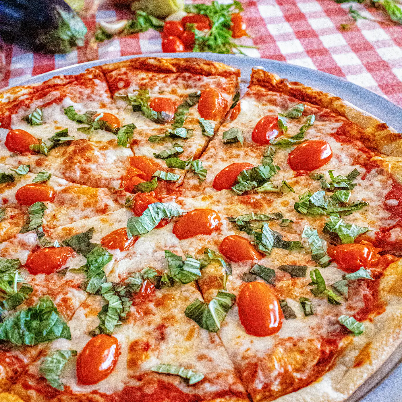A whole Margarita pizza with cherry tomatoes and basil on the checkered cloth
