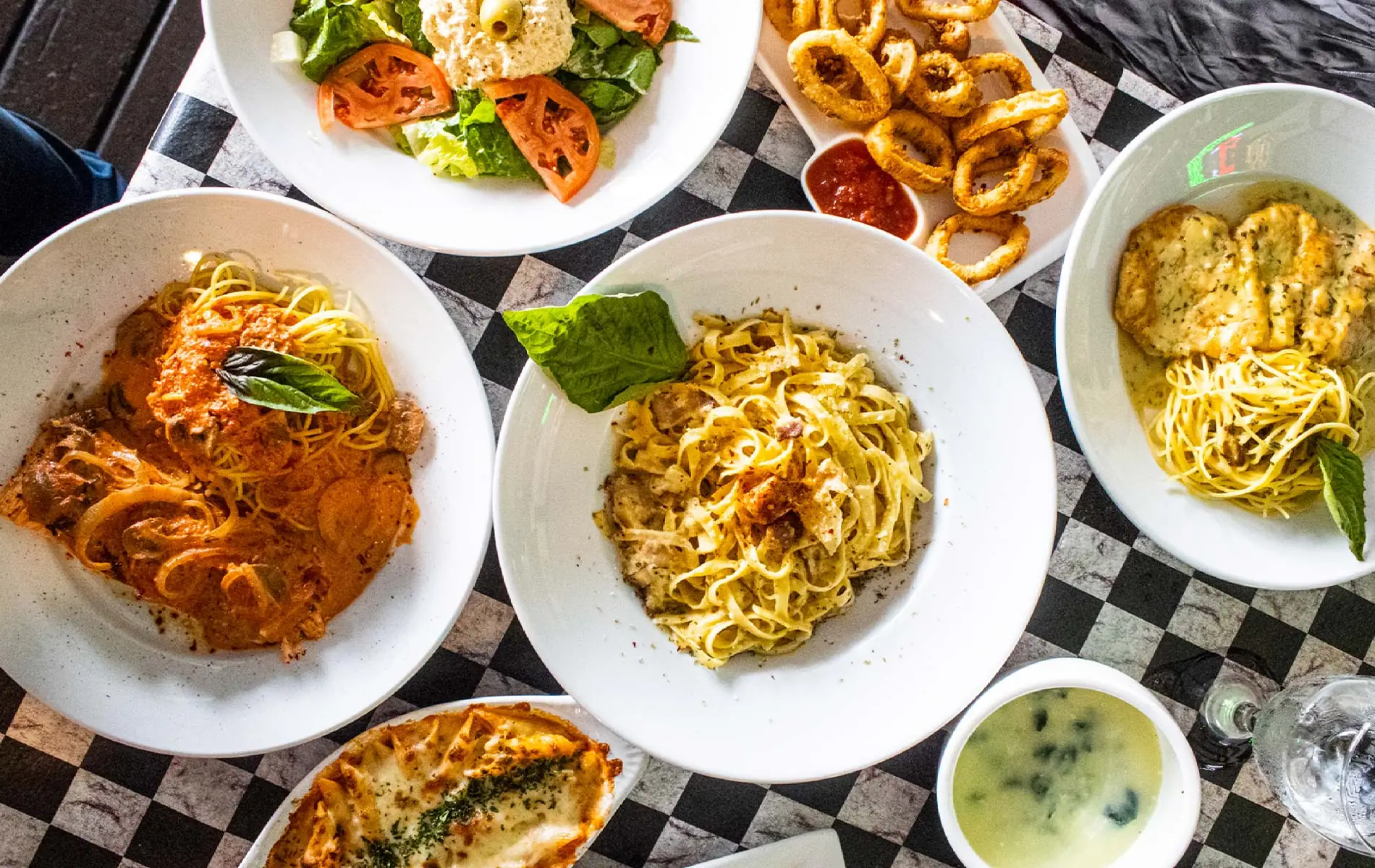 A full table of Di Papa's dishes shot from overhead, on the restaurant's red and white checkered cloth